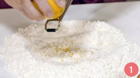 Sul piano di lavoro disponiamo la farina a fontana e al centro grattugiamo la scorza di limone